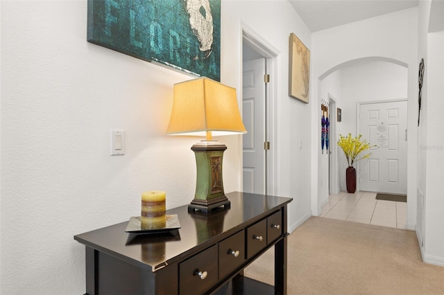 hall with light tile patterned floors, baseboards, arched walkways, and light colored carpet