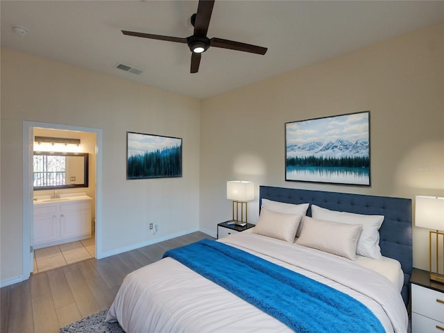 bedroom with visible vents, ensuite bathroom, a sink, wood finished floors, and baseboards