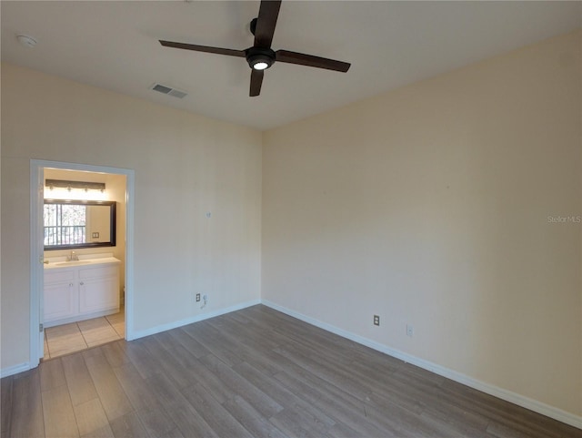 unfurnished bedroom featuring a sink, wood finished floors, visible vents, baseboards, and ensuite bath