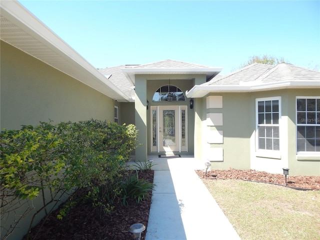 view of exterior entry with a shingled roof and stucco siding