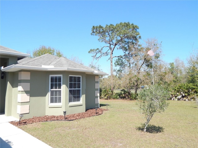 view of home's exterior featuring roof with shingles, a yard, and stucco siding