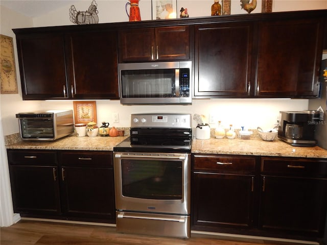 kitchen with a toaster, light stone countertops, appliances with stainless steel finishes, dark brown cabinets, and wood finished floors