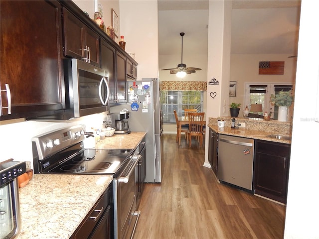 kitchen featuring stainless steel appliances, dark brown cabinetry, light stone counters, and wood finished floors