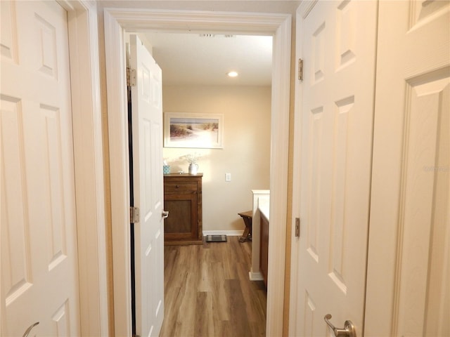 hall featuring light wood finished floors, baseboards, and recessed lighting