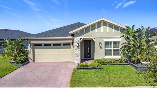 view of front of house with a shingled roof, stone siding, an attached garage, decorative driveway, and a front yard