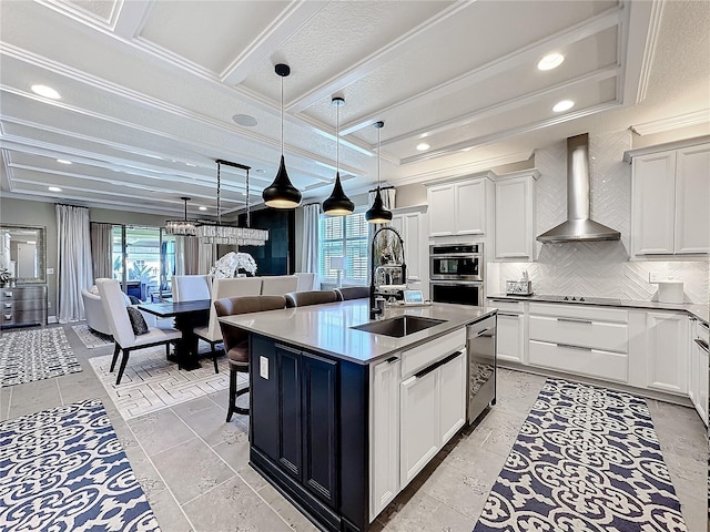 kitchen with decorative backsplash, wall chimney exhaust hood, appliances with stainless steel finishes, hanging light fixtures, and a sink