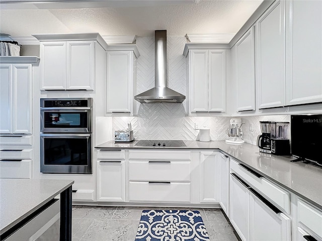 kitchen featuring white cabinets, wall chimney exhaust hood, black electric stovetop, stainless steel double oven, and backsplash