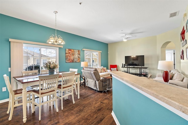 dining space featuring arched walkways, ceiling fan with notable chandelier, visible vents, baseboards, and dark wood-style floors