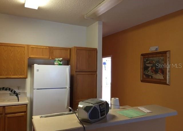 kitchen with brown cabinets, freestanding refrigerator, light countertops, a textured ceiling, and a sink