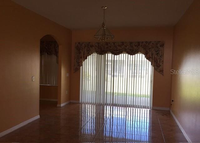 tiled spare room featuring baseboards and arched walkways