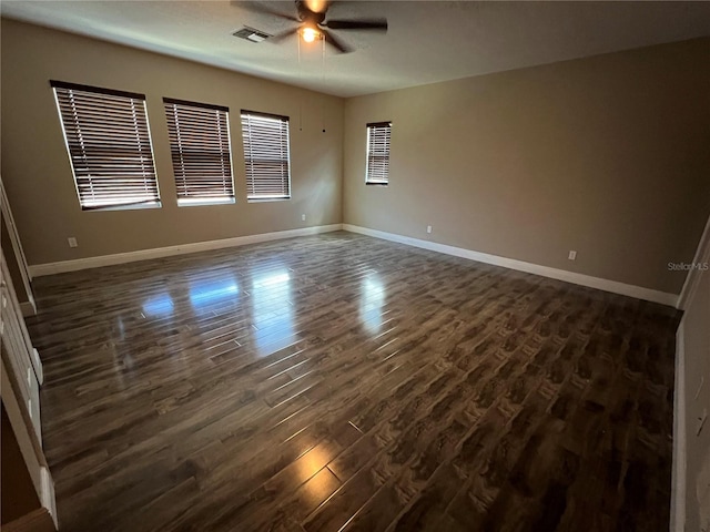 empty room with baseboards, ceiling fan, visible vents, and dark wood-style flooring