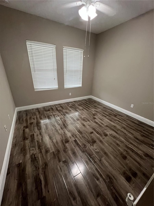 empty room with dark wood-style flooring, a ceiling fan, and baseboards