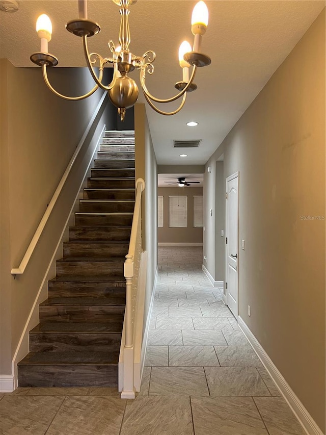 stairs featuring visible vents, baseboards, and ceiling fan with notable chandelier