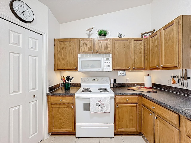 kitchen with light tile patterned floors, white appliances, dark countertops, and brown cabinets