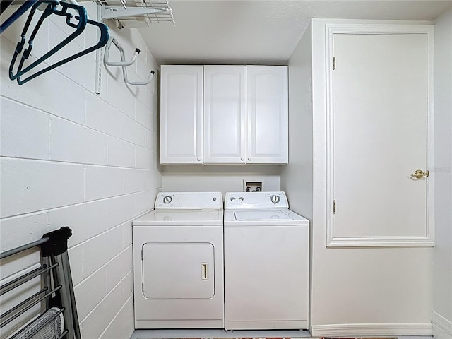 clothes washing area featuring washing machine and dryer, cabinet space, and concrete block wall