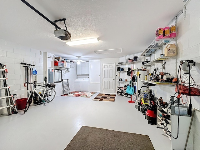 garage featuring concrete block wall, electric panel, a garage door opener, and independent washer and dryer