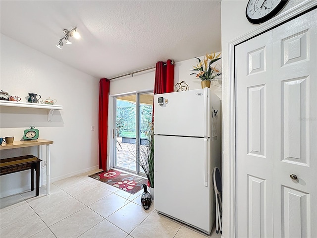 kitchen with a textured ceiling, light tile patterned floors, freestanding refrigerator, and baseboards