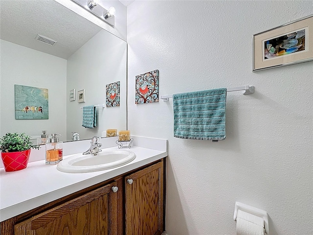 bathroom with a textured ceiling, vanity, and visible vents