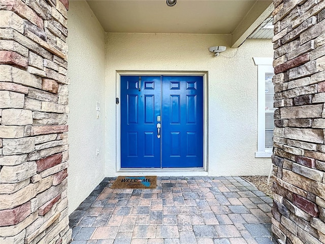 view of exterior entry with stucco siding and stone siding