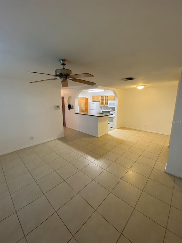 unfurnished living room with light tile patterned floors, ceiling fan, arched walkways, visible vents, and baseboards