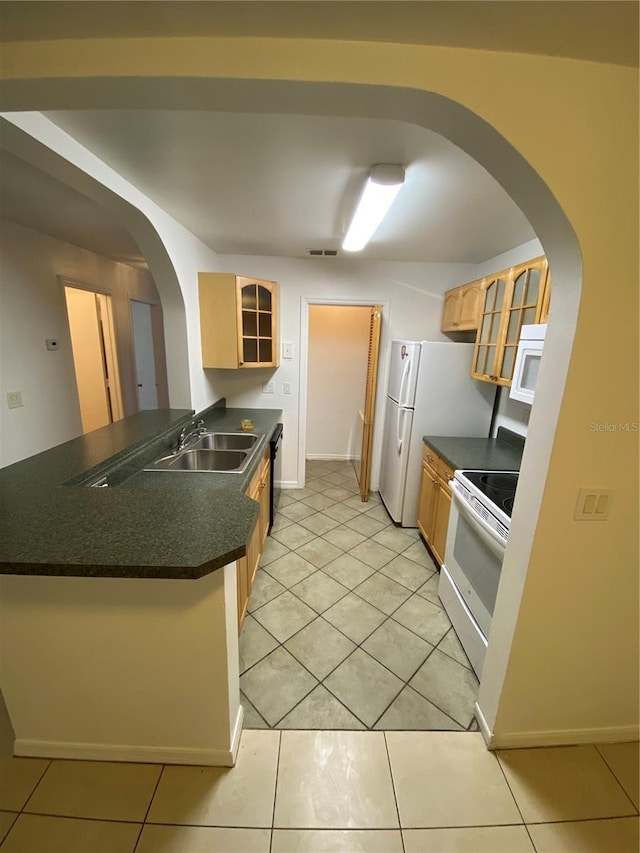 kitchen with dark countertops, glass insert cabinets, a sink, white appliances, and a peninsula