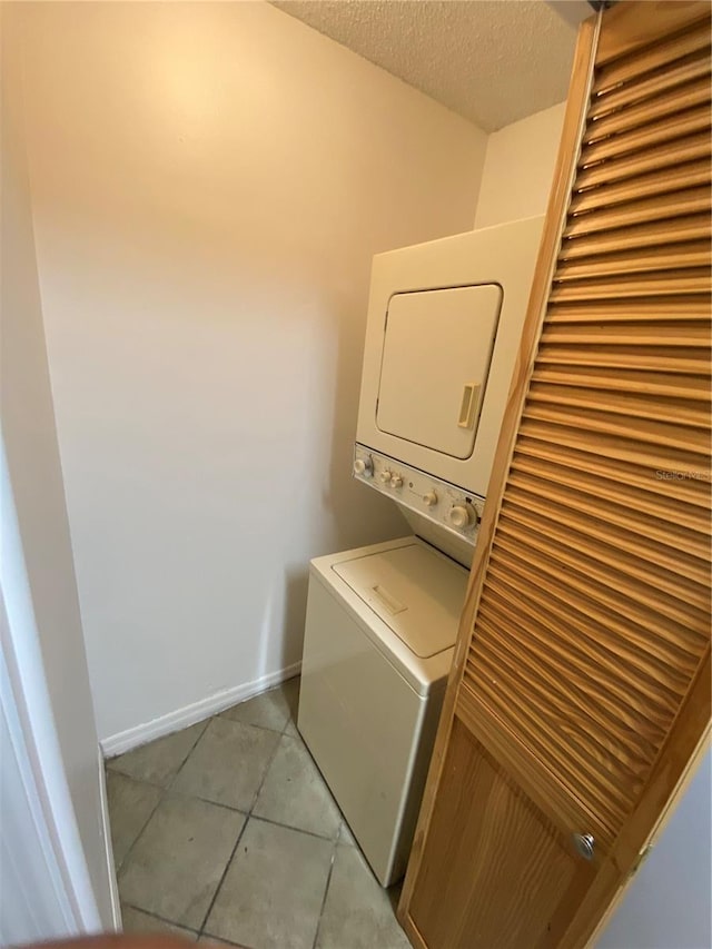 laundry area featuring light tile patterned floors, stacked washer / drying machine, a textured ceiling, laundry area, and baseboards