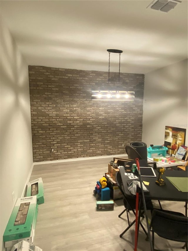 interior space with brick wall, wood finished floors, visible vents, and baseboards