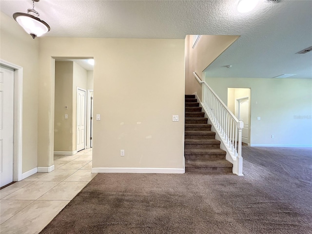 spare room with light carpet, baseboards, stairway, and a textured ceiling