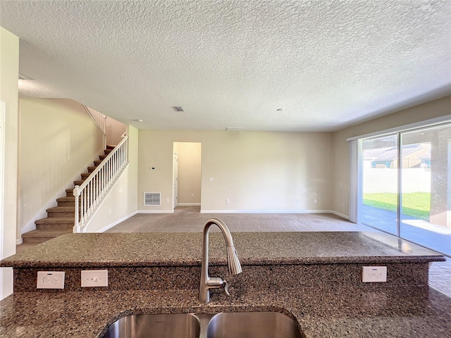 kitchen with a sink, visible vents, baseboards, dark stone countertops, and carpet