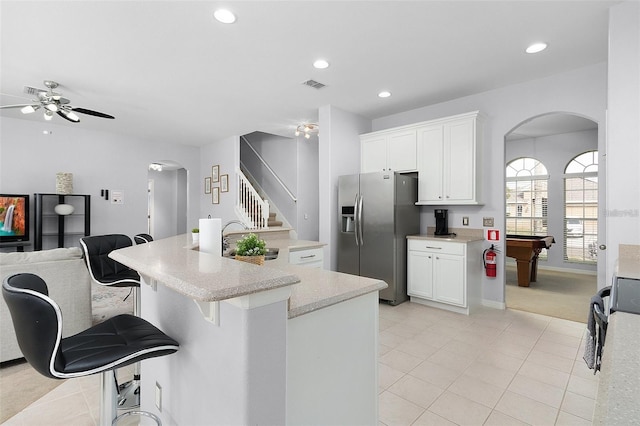 kitchen with arched walkways, visible vents, stainless steel fridge, and white cabinetry