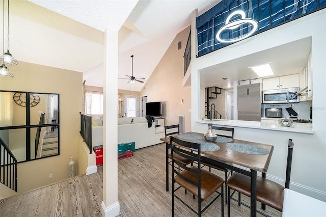 dining area with ceiling fan, high vaulted ceiling, wood finished floors, visible vents, and stairs