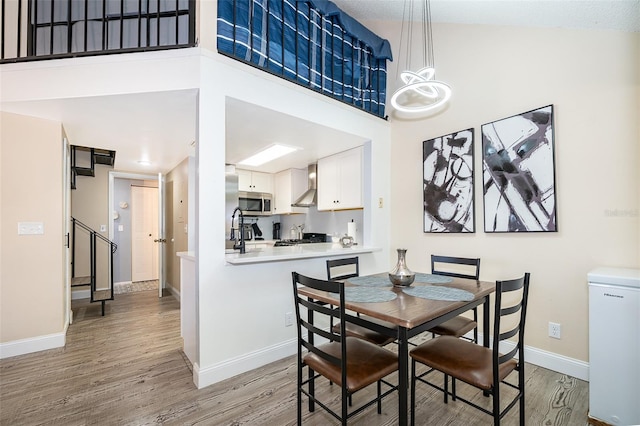 dining area featuring light wood-style flooring, a high ceiling, baseboards, and stairs