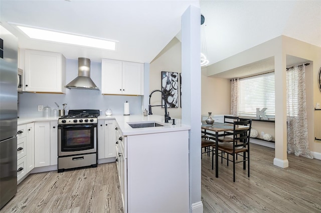 kitchen with light wood-style flooring, stainless steel appliances, light countertops, wall chimney range hood, and a sink