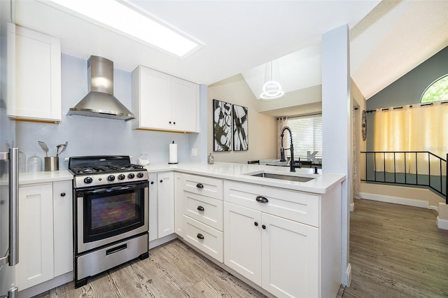 kitchen featuring light wood-style flooring, a sink, vaulted ceiling, wall chimney range hood, and gas range