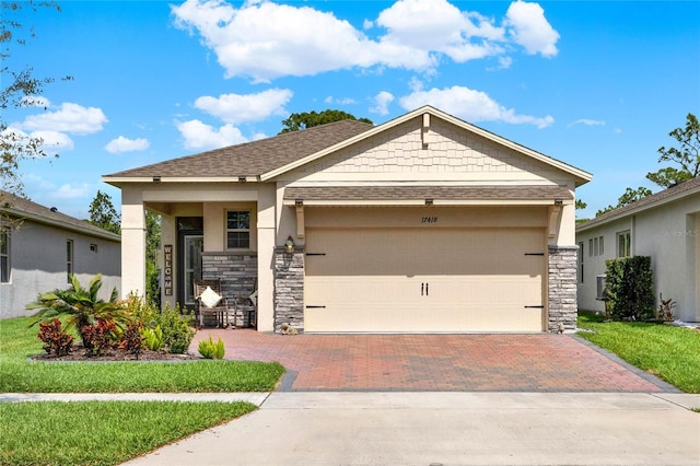 view of front facade with stone siding, a front yard, decorative driveway, and a garage