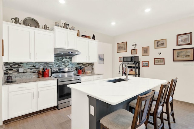 kitchen featuring a breakfast bar area, a center island with sink, a sink, stainless steel appliances, and under cabinet range hood