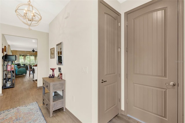 hall with baseboards, light wood-type flooring, and a chandelier