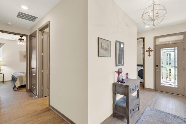 entrance foyer with visible vents, baseboards, light wood-style flooring, a notable chandelier, and washer / clothes dryer