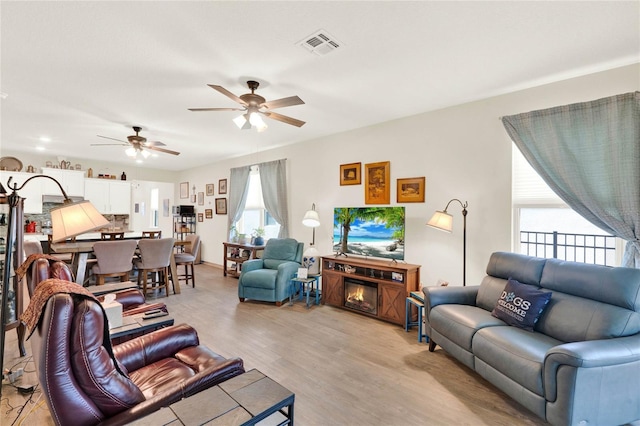 living area featuring light wood finished floors, visible vents, ceiling fan, and a glass covered fireplace