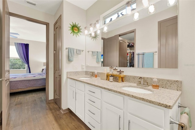 ensuite bathroom featuring visible vents, connected bathroom, double vanity, wood finished floors, and a sink