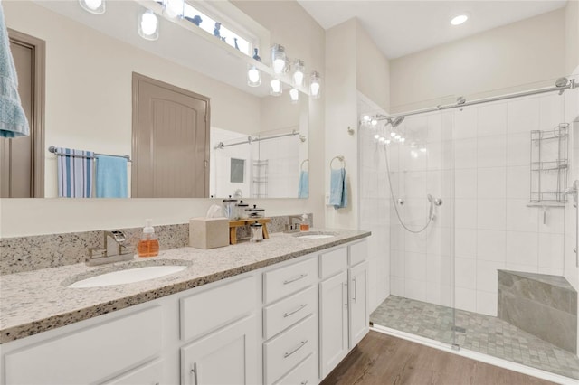 full bath with a sink, double vanity, wood finished floors, and a shower stall