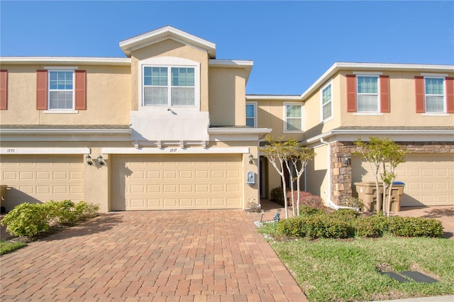 townhome / multi-family property with a garage, decorative driveway, and stucco siding