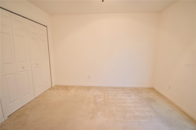 unfurnished bedroom featuring baseboards, a closet, and light colored carpet