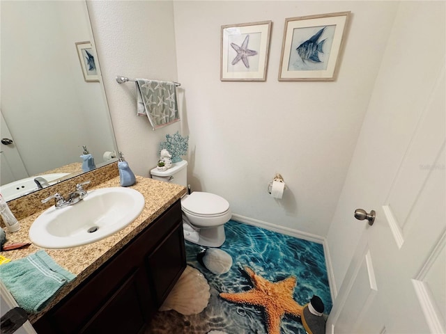 half bath featuring baseboards, vanity, and toilet