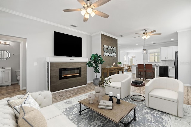 living room with visible vents, baseboards, ornamental molding, light wood finished floors, and a glass covered fireplace