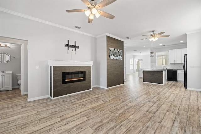 unfurnished living room with light wood finished floors, baseboards, visible vents, a glass covered fireplace, and ornamental molding