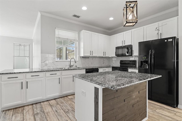 kitchen with a sink, ornamental molding, light wood-type flooring, dark stone counters, and black appliances