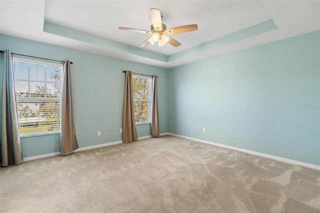 carpeted spare room with baseboards, a tray ceiling, and ceiling fan