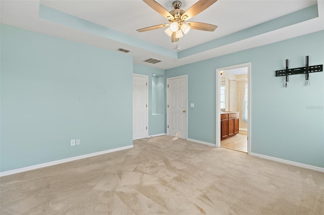 unfurnished bedroom featuring light carpet, a tray ceiling, visible vents, and baseboards