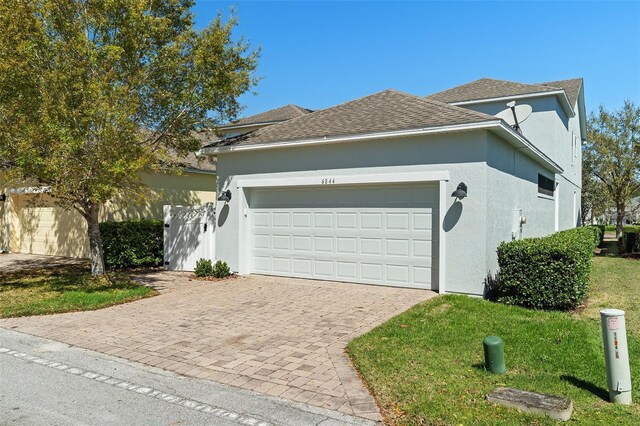 view of front facade with a garage, roof with shingles, decorative driveway, a front lawn, and stucco siding